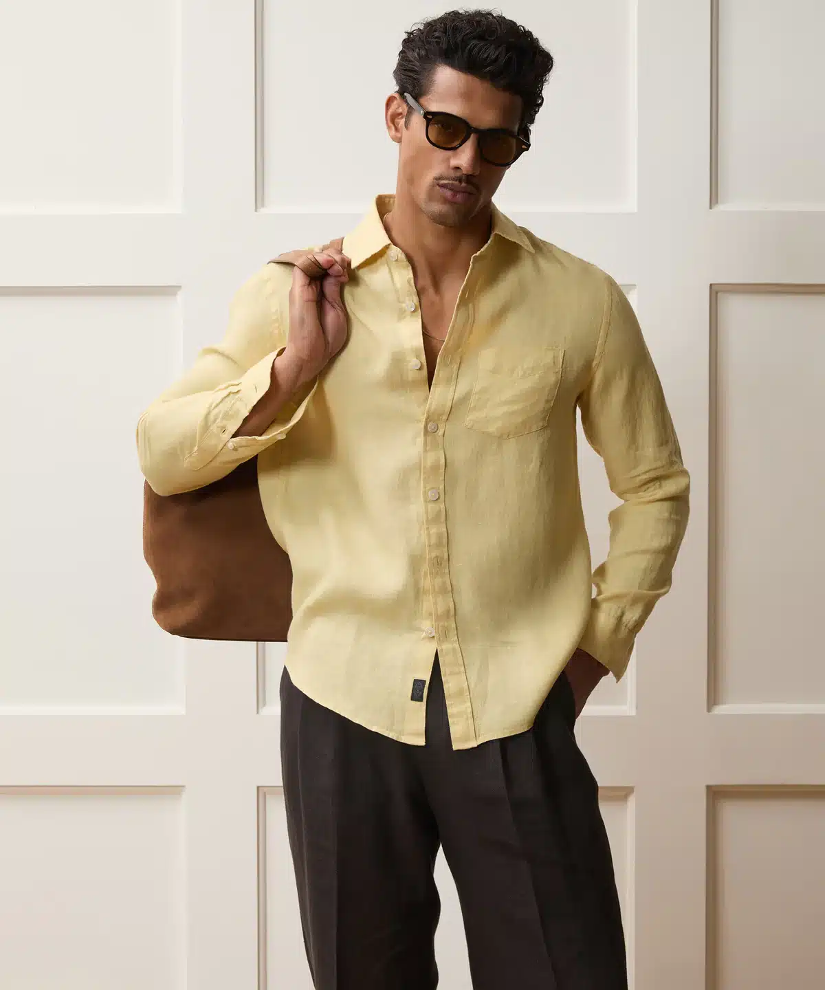 Man wearing a butter yellow linen point collar shirt with brown linen trousers and a suede tote