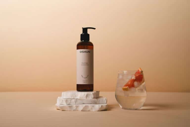 Amber pump bottle on stone next to a glass of water with fruit