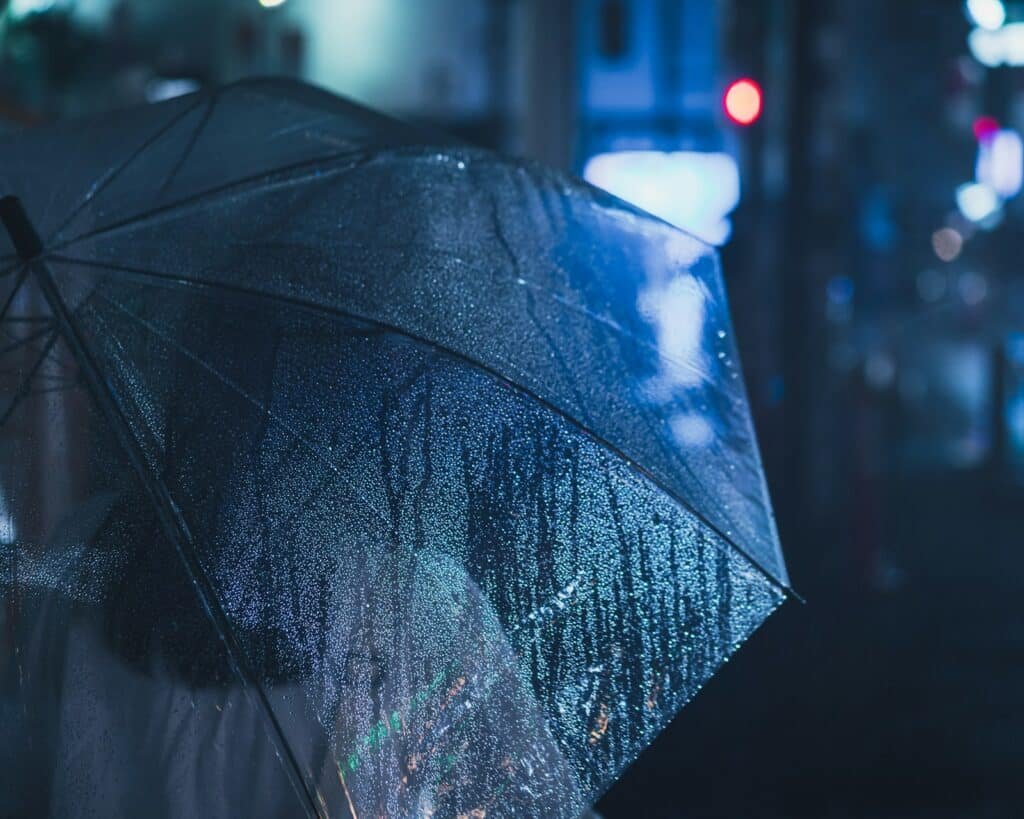 Black umbrella covered in raindrops on a city street at night