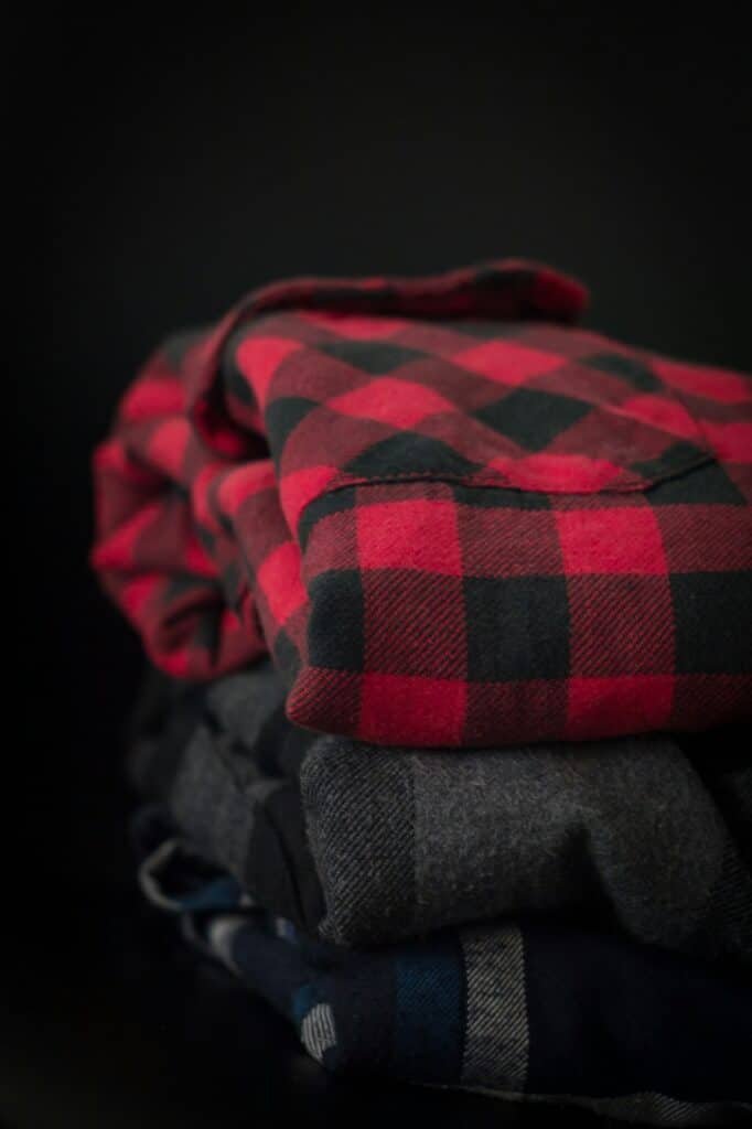 Folded red and black buffalo check flannel shirts stacked on a dark surface