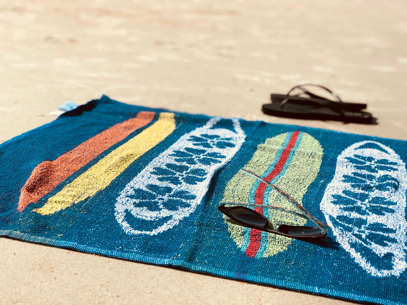 Colorful beach towel with sunglasses and flip-flops on the sand