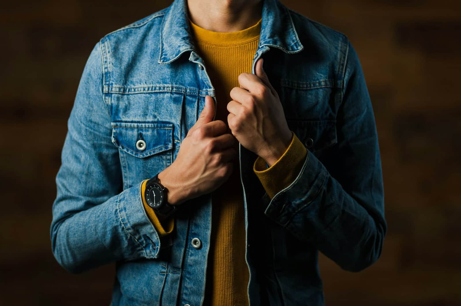 Man buttoning a blue denim jacket over a mustard t-shirt