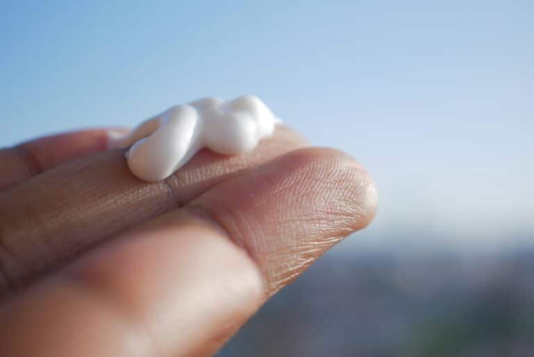 Dollop of white cream on a fingertip against a blue sky