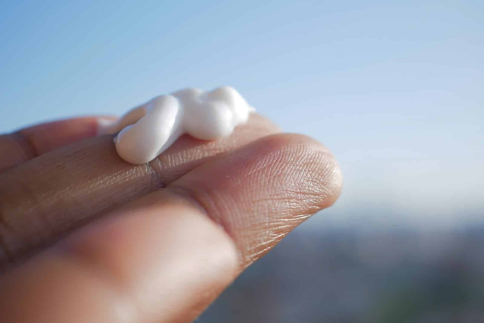 Dollop of white cream on a fingertip against a blue sky