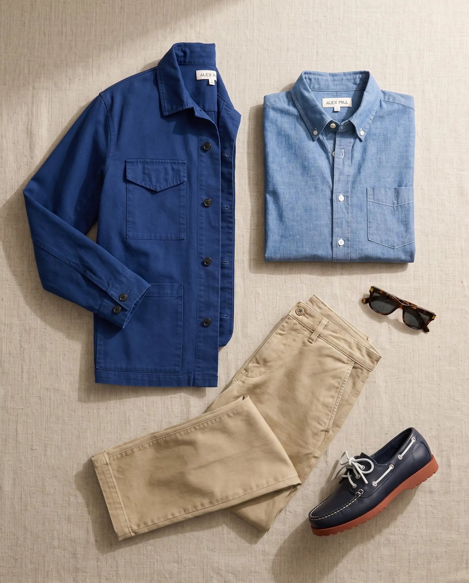 Flat lay of the Alex Mill chore jacket, chambray shirt, faded khaki chino and Quoddy boat shoes