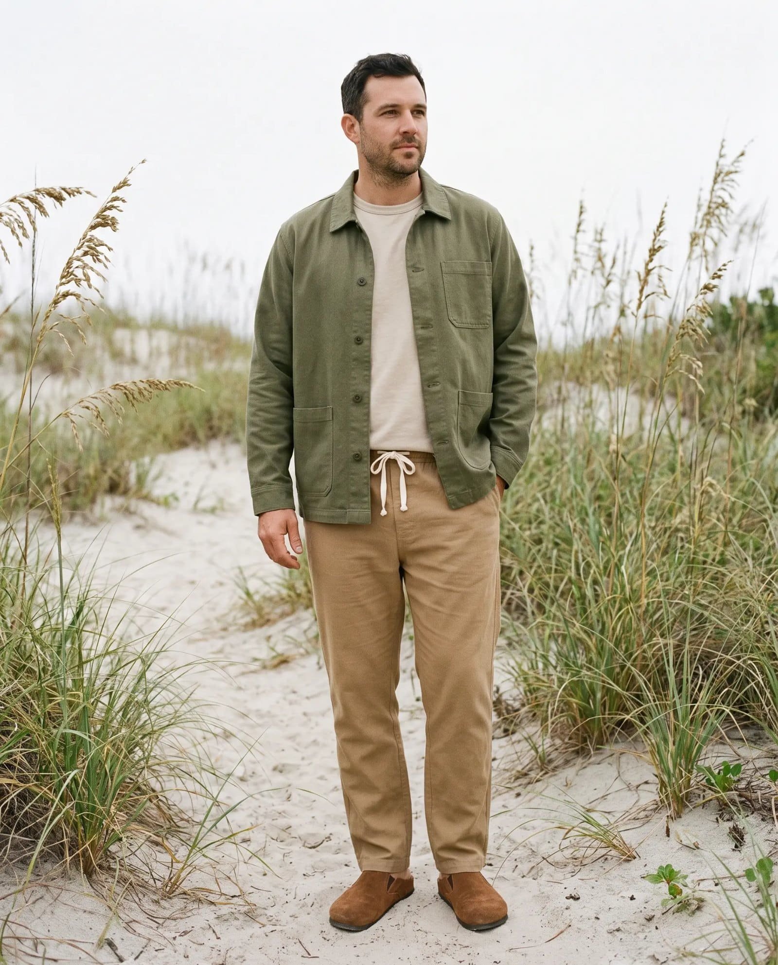 Man in the Jungmaven Olympic hemp jacket in olive over a stucco Baja tee with coyote hemp pants on a dune path