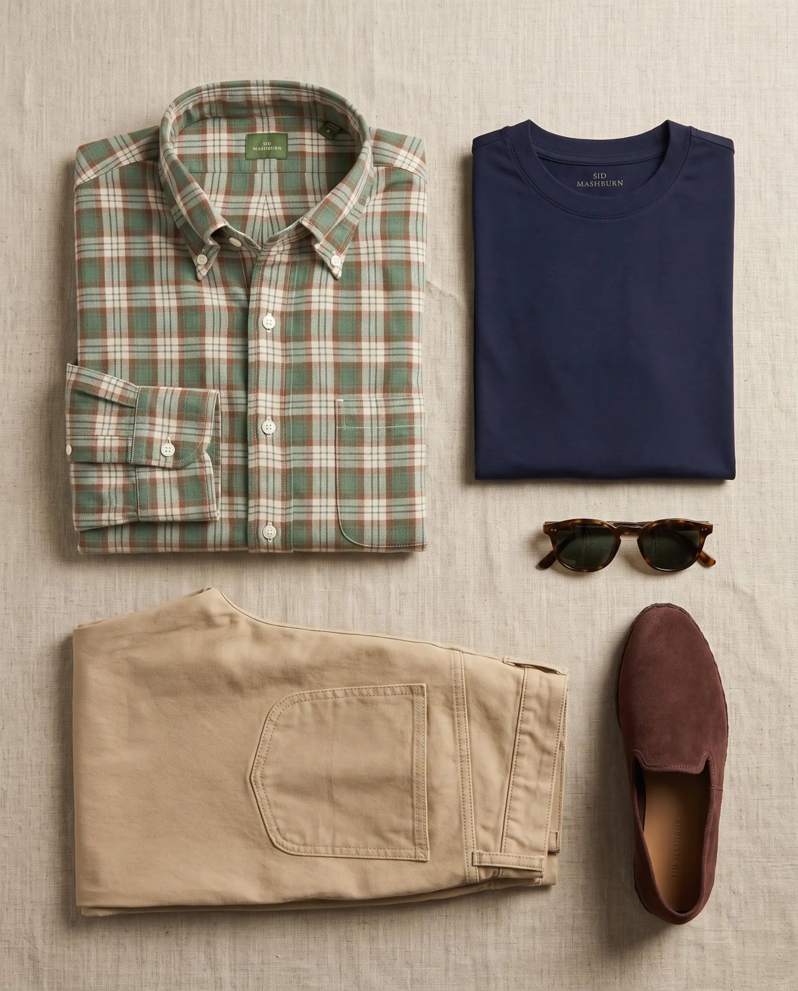 Flat lay of the Sid Mashburn madras shirt, navy pima tee, khaki brush pant and Sabah slip-ons