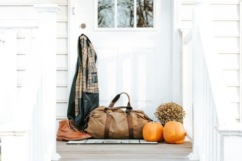 Plaid shirt on a coat hook beside a canvas duffel bag, leather boots and pumpkins on a front porch