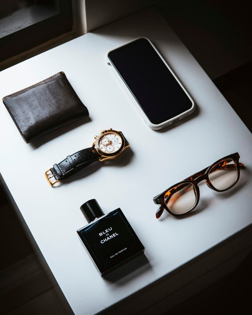 Flat lay of a wallet, watch, glasses, phone and a cologne bottle