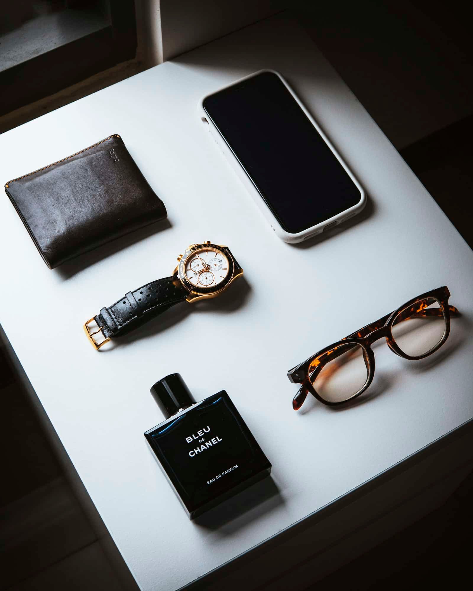 Flat lay of a wallet, watch, glasses, phone and a cologne bottle