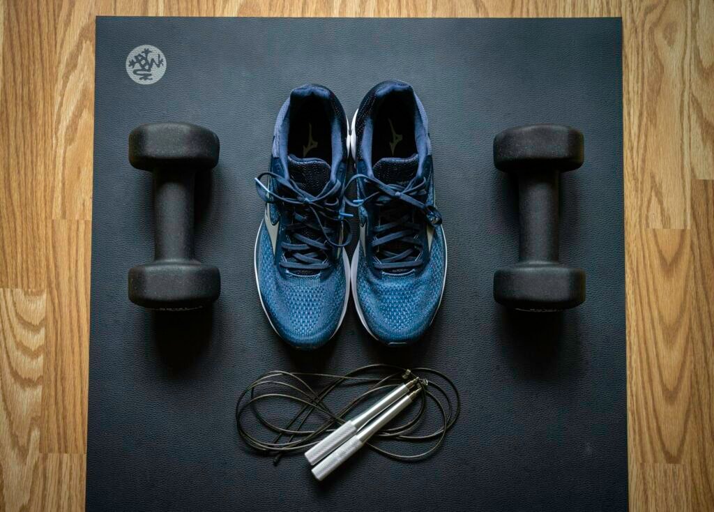 Flat lay of running shoes, dumbbells and a jump rope on an exercise mat