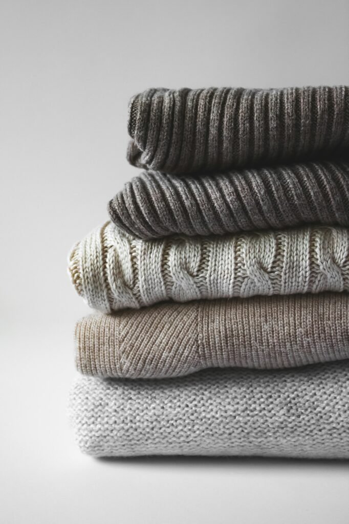 Stack of folded grey and cream cable knit sweaters