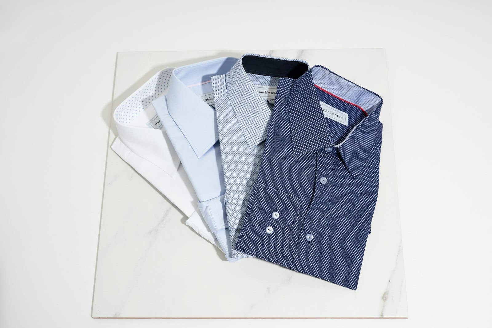 Folded dress shirts in white, light blue and navy print on a marble board