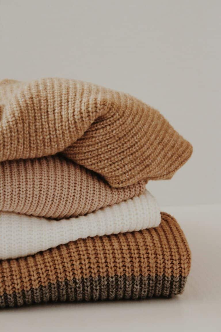 Stack of folded knit sweaters in camel, cream and brown