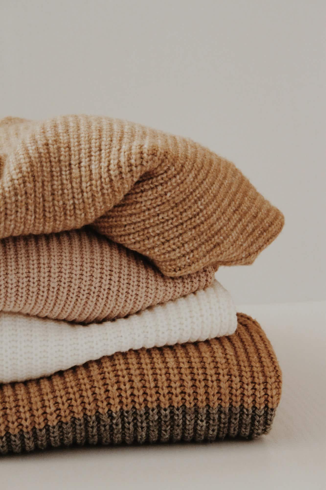 Stack of folded knit sweaters in camel, cream and brown