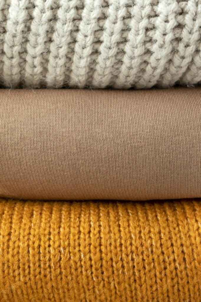 Folded knit sweaters stacked in cream, tan and mustard