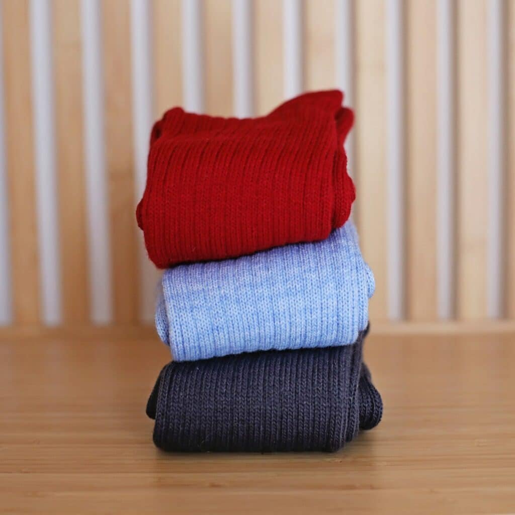 Folded ribbed socks in red, light blue and navy stacked on a wooden table