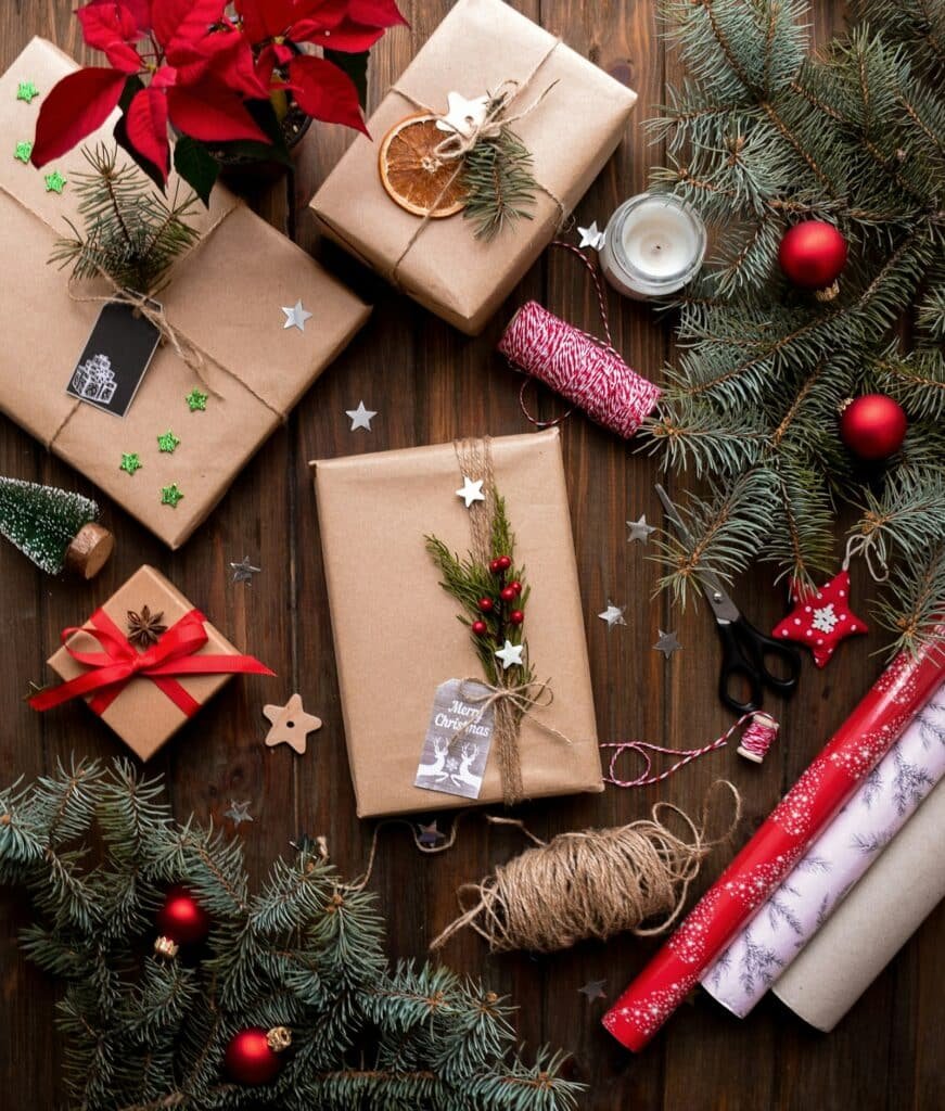 Gifts wrapped in brown kraft paper with twine, evergreen and red ornaments, seen from above