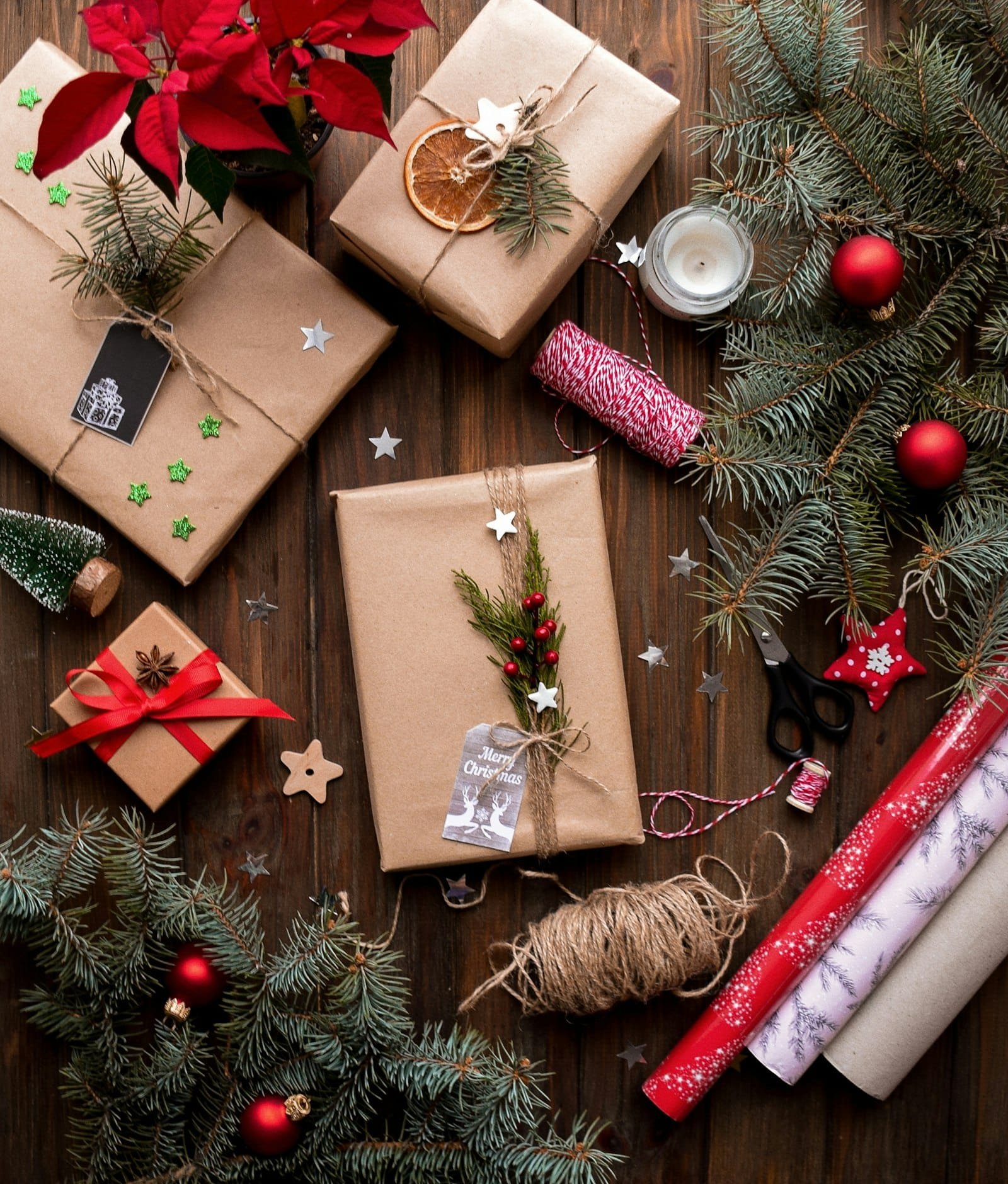 Gifts wrapped in brown kraft paper with twine, evergreen and red ornaments, seen from above
