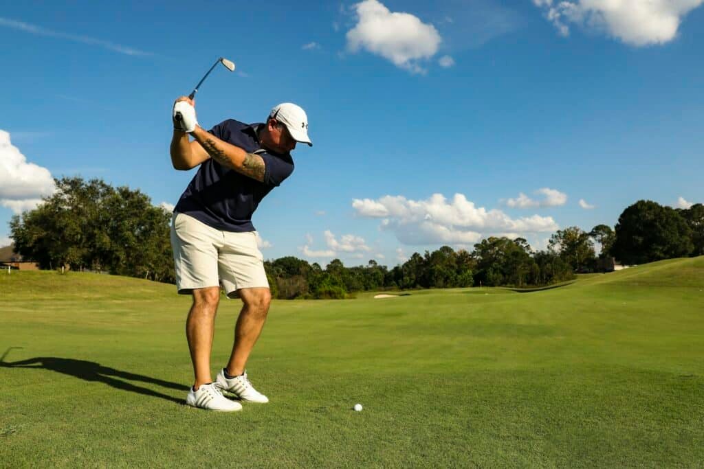 Golfer in a black shirt and white shorts mid-swing on a course