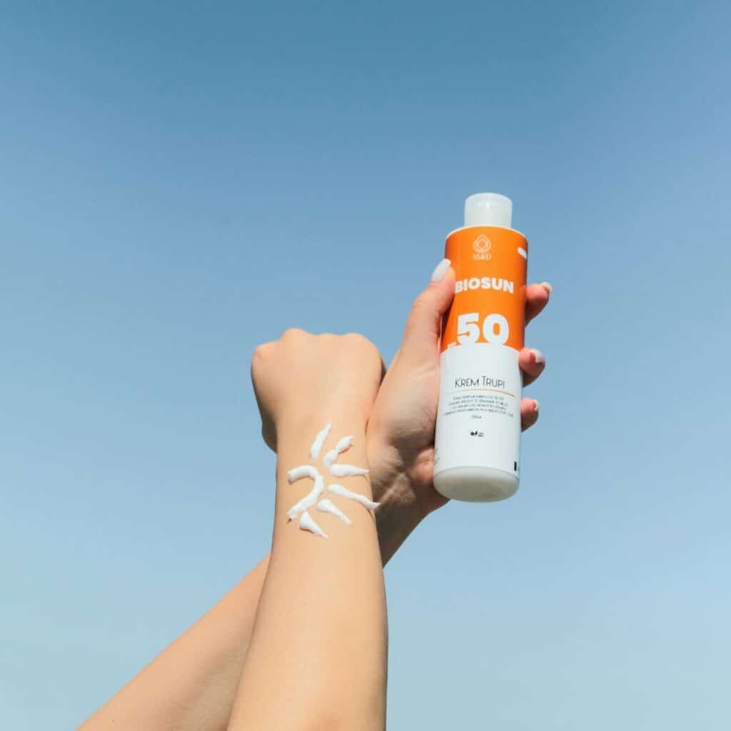 Hand holding an SPF 50 sunscreen bottle with a stripe of sunscreen on the wrist