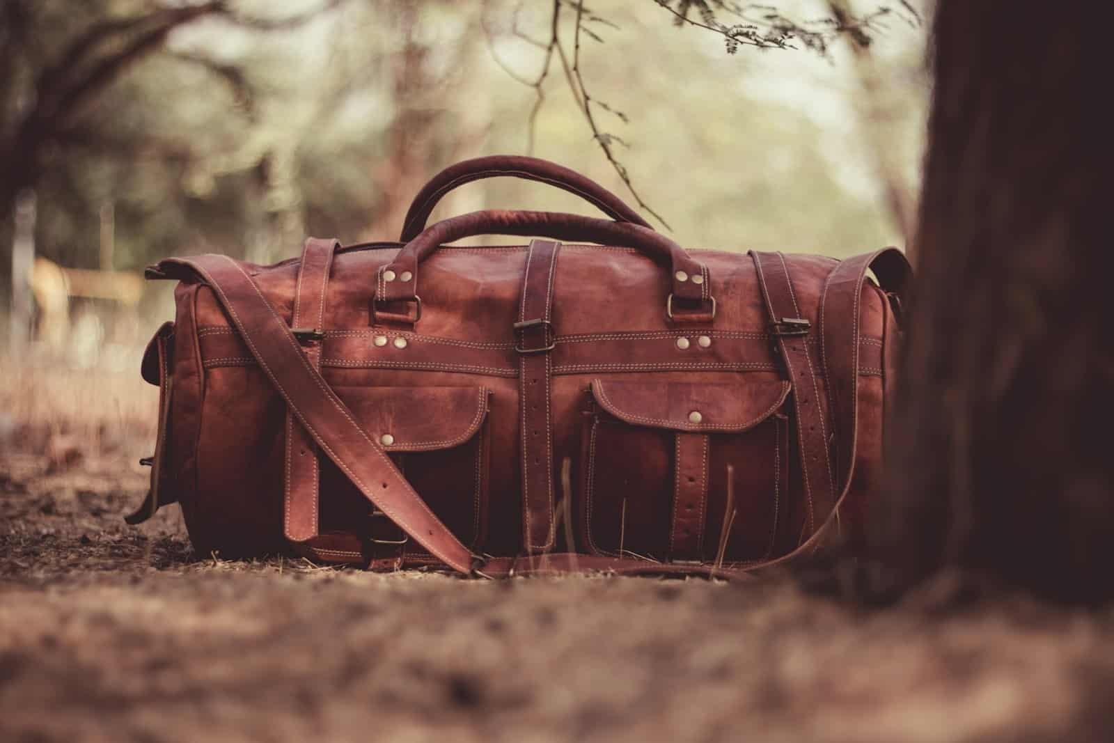 Brown leather duffle bag on the forest floor beside a tree