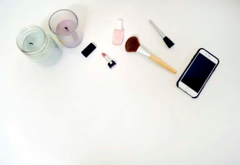 Makeup brushes, lipstick, nail polish, candles and a phone on a white surface