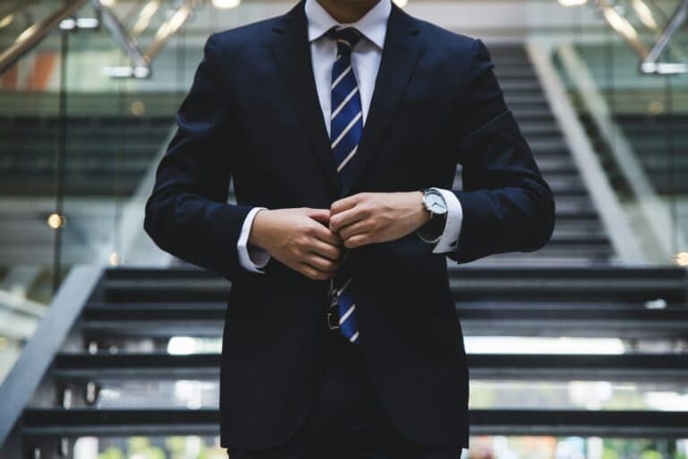 Man buttoning a navy suit jacket over a white shirt and striped tie