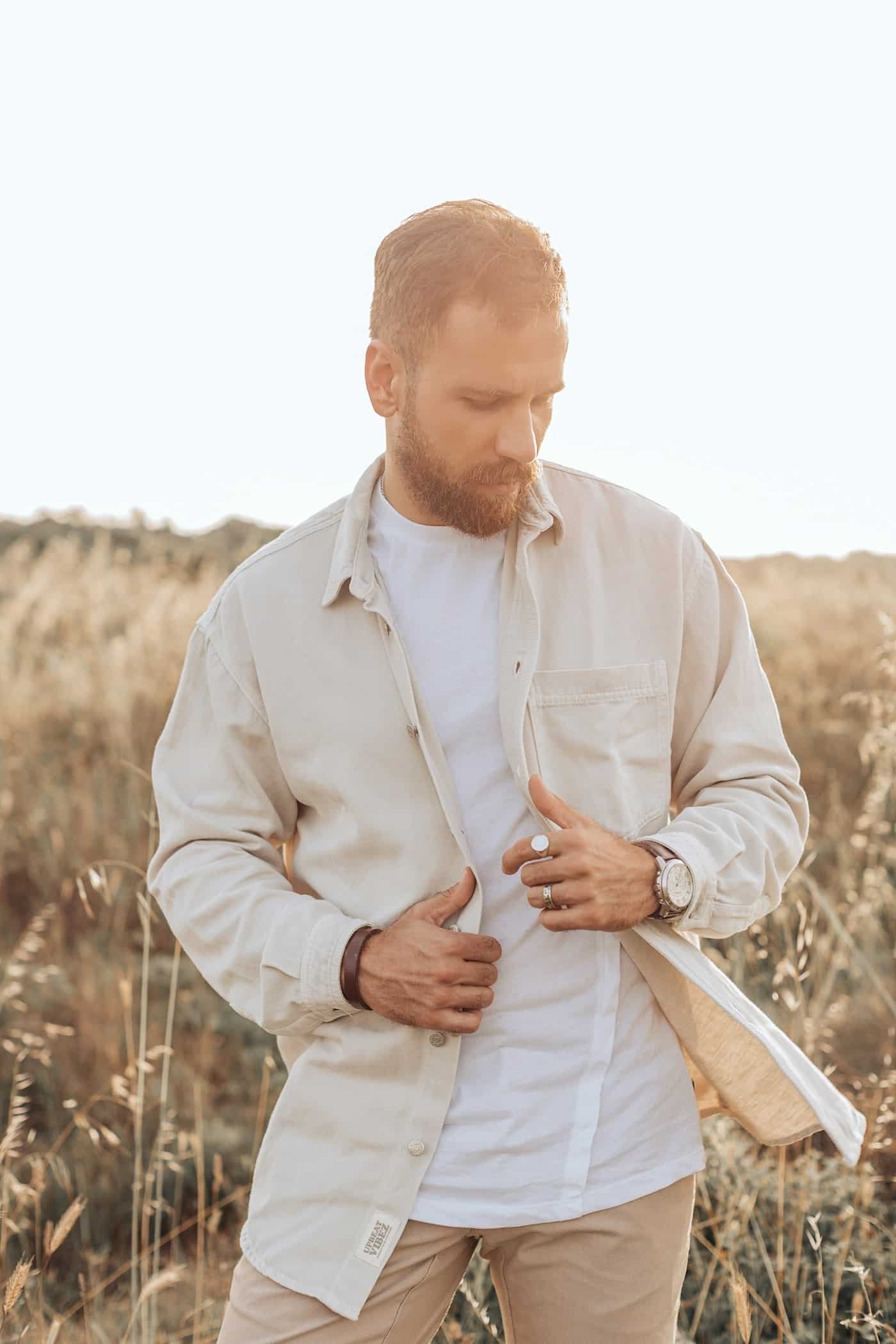 Man in an open cream overshirt over a white tee in a sunlit field