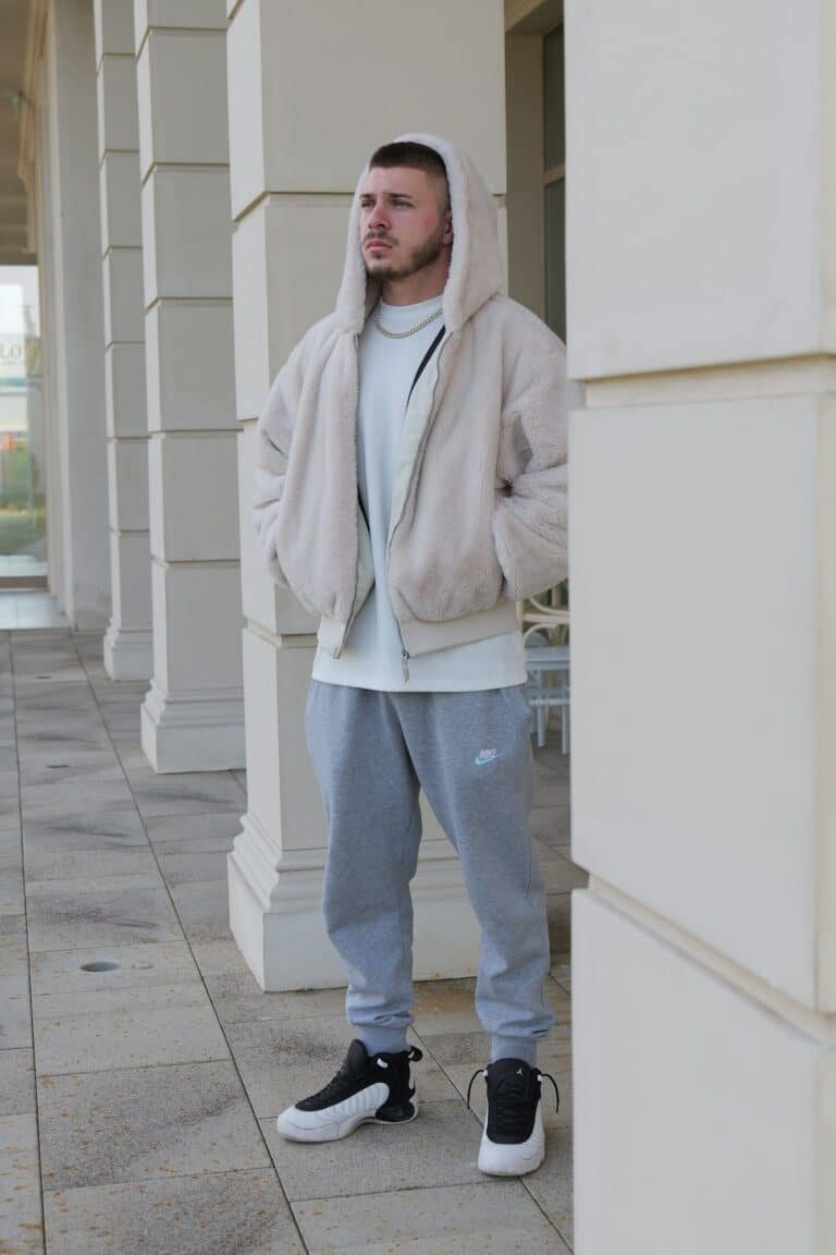 Man in a beige fleece hoodie and grey sweatpants between white pillars
