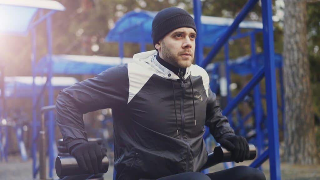 Man in a black and white jacket and beanie working out at an outdoor gym