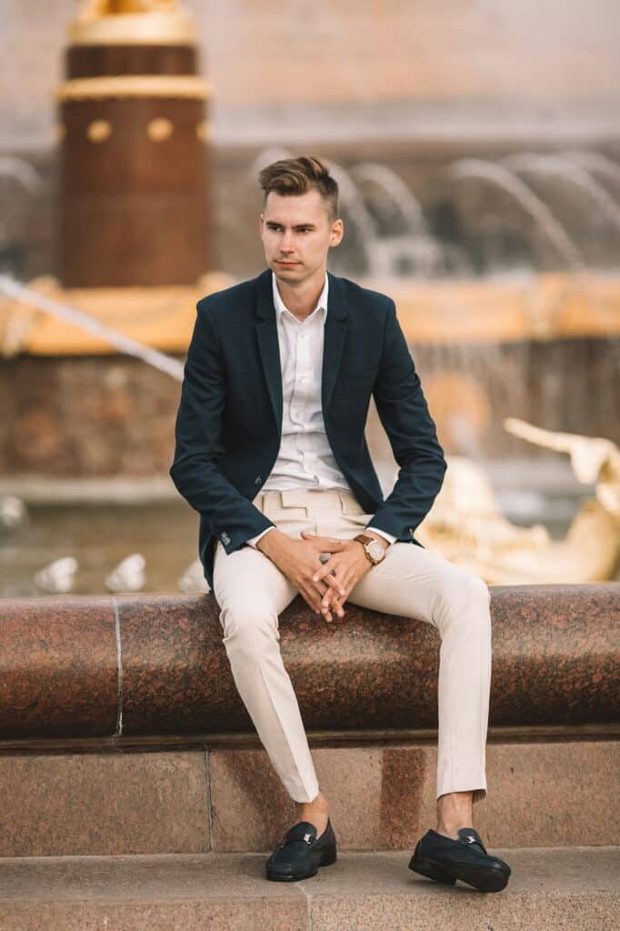 Man in a black blazer and cream trousers sitting on a concrete bench