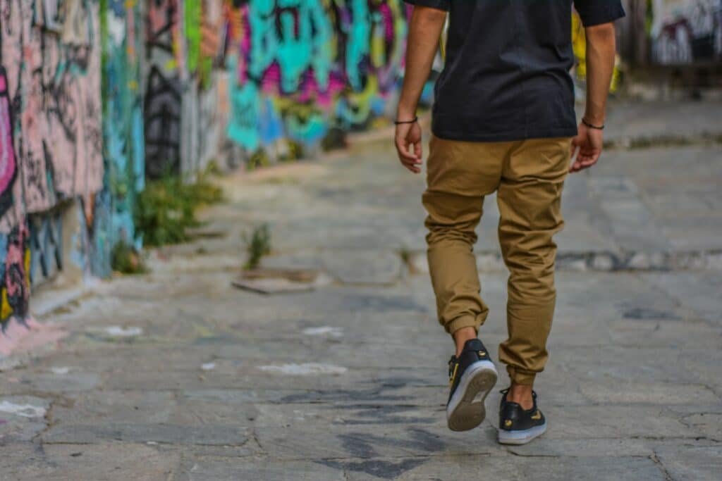 Man in a black shirt and khaki joggers walking beside a graffiti wall