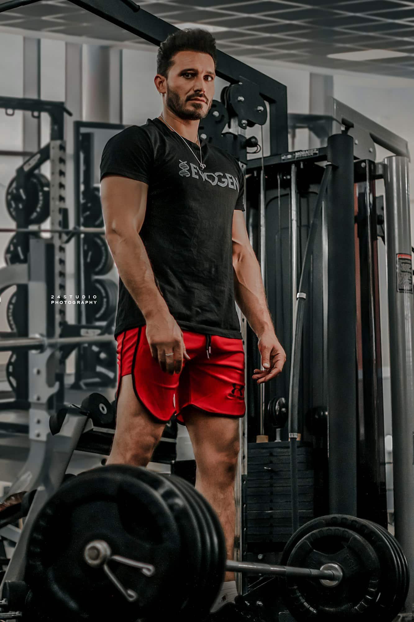 Man in a black t-shirt and red shorts in front of a gym machine