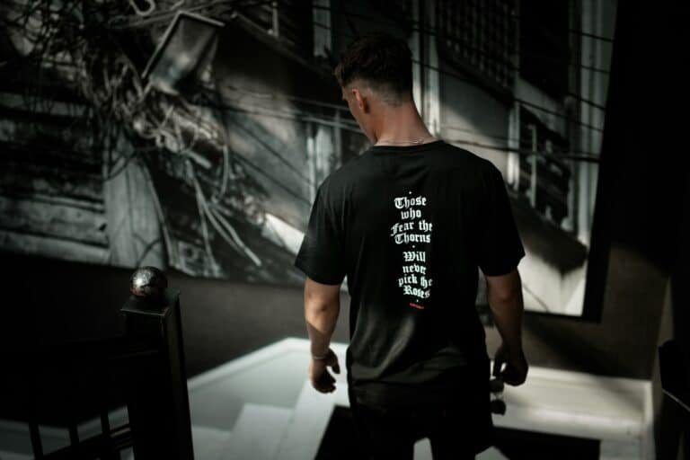 Man in a black t-shirt looking down a staircase in a gym