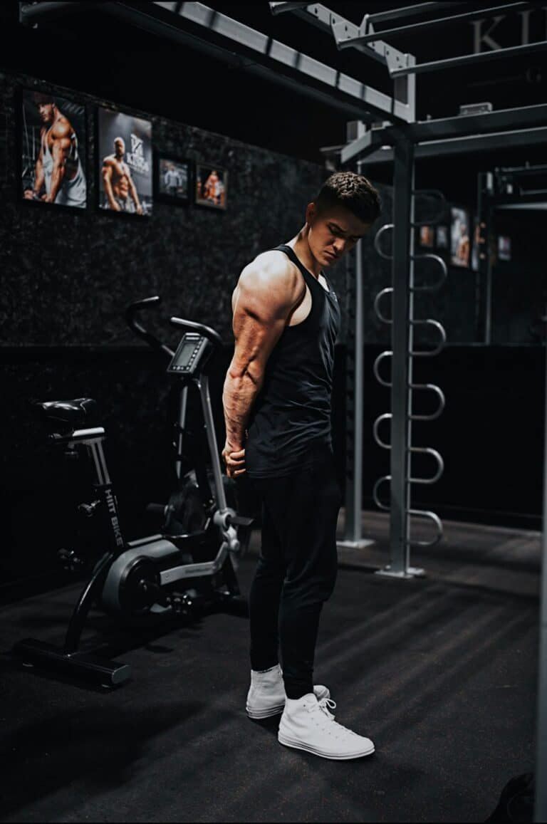 Man in a black tank top and black pants standing on gym equipment