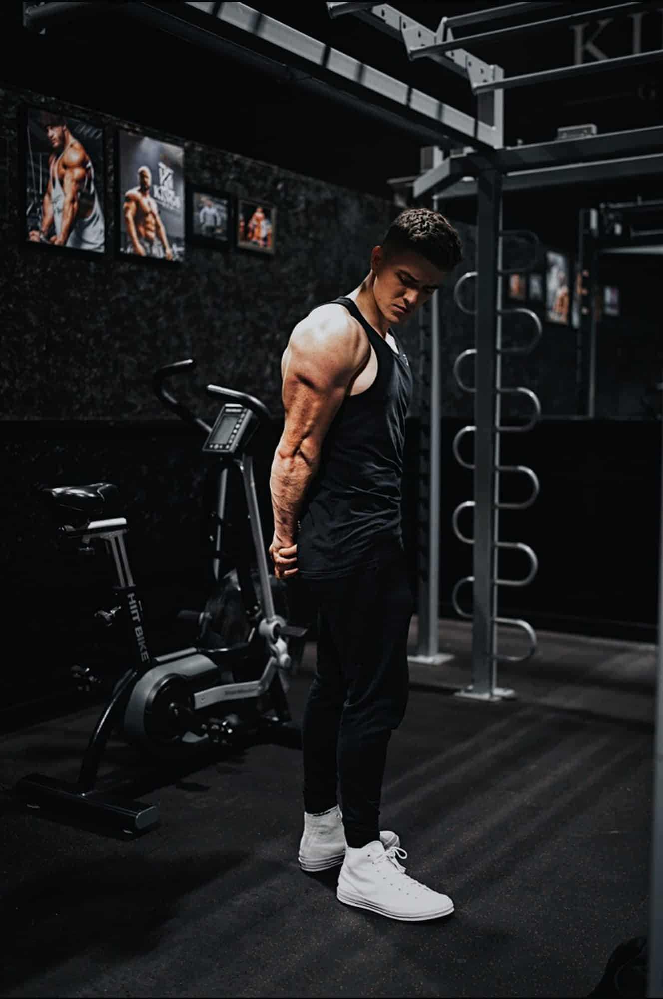 Man in a black tank top and black pants standing on gym equipment