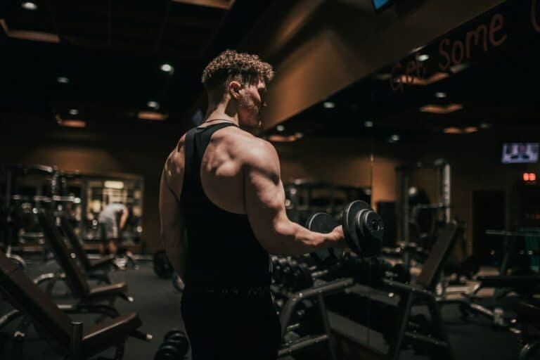 Man in a black tank top doing a dumbbell curl in a dark gym