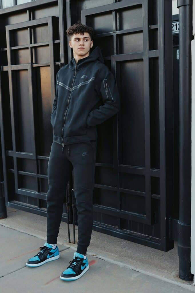 Man in a black tracksuit and sneakers standing by a doorway