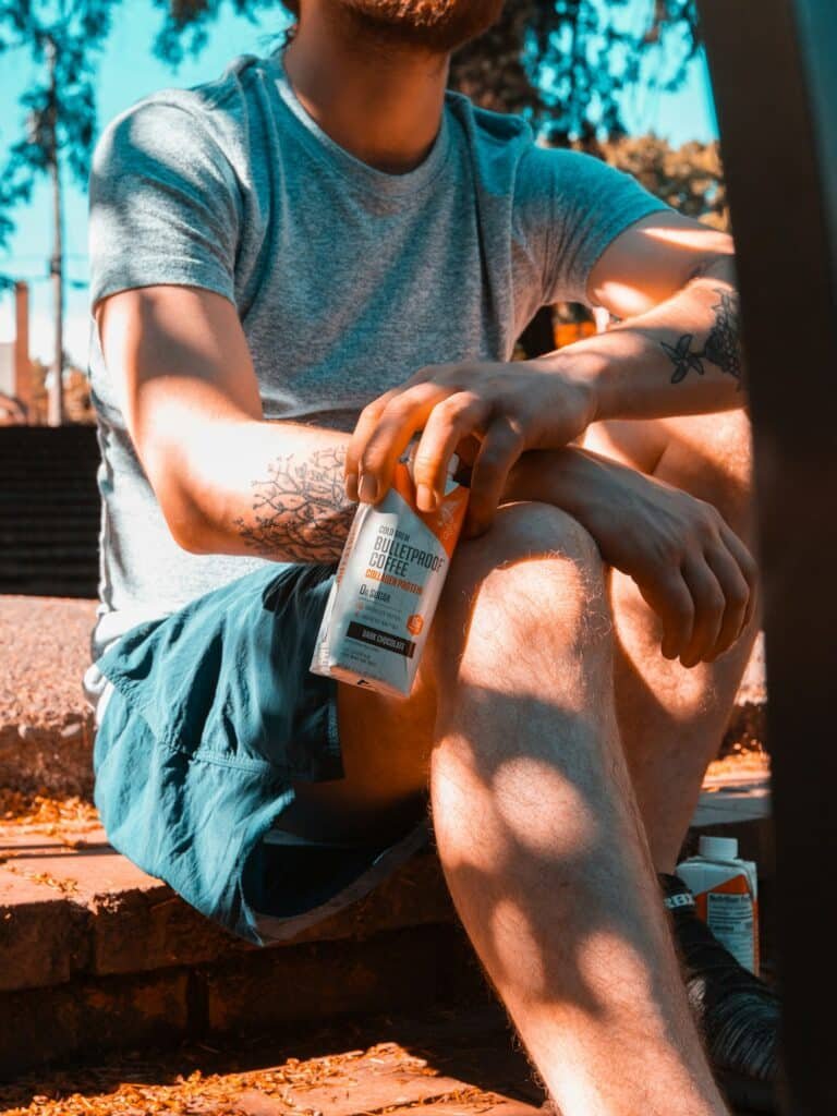 Man in a gray tee and shorts sitting in the sun holding a white and orange tube
