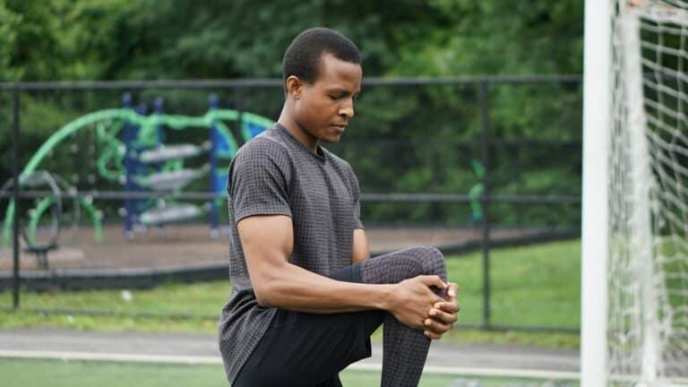 Man in a gray tee stretching on one knee in a park