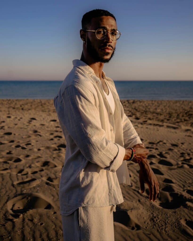 Man in a light linen shirt and trousers on a sandy beach at sunset