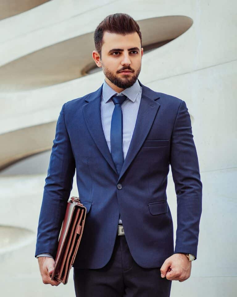 Man in a navy suit and blue tie holding a brown leather bag