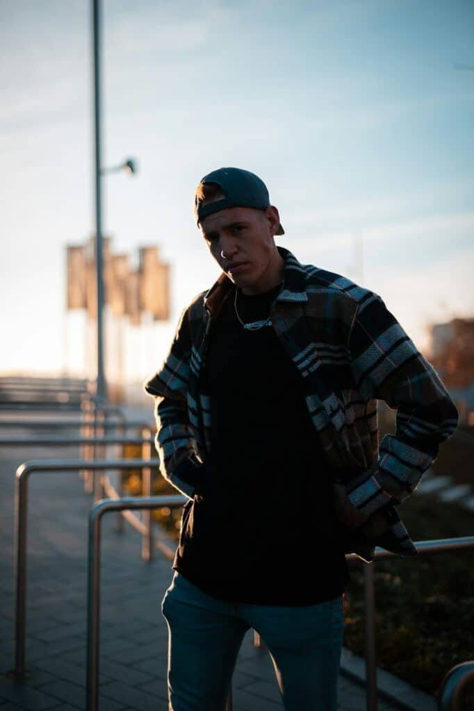 Man in a plaid overshirt and cap standing on a dock at sunset