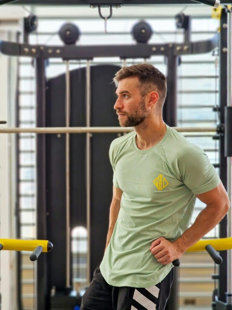Man in a sage green t-shirt standing in a gym with his hands on his hips
