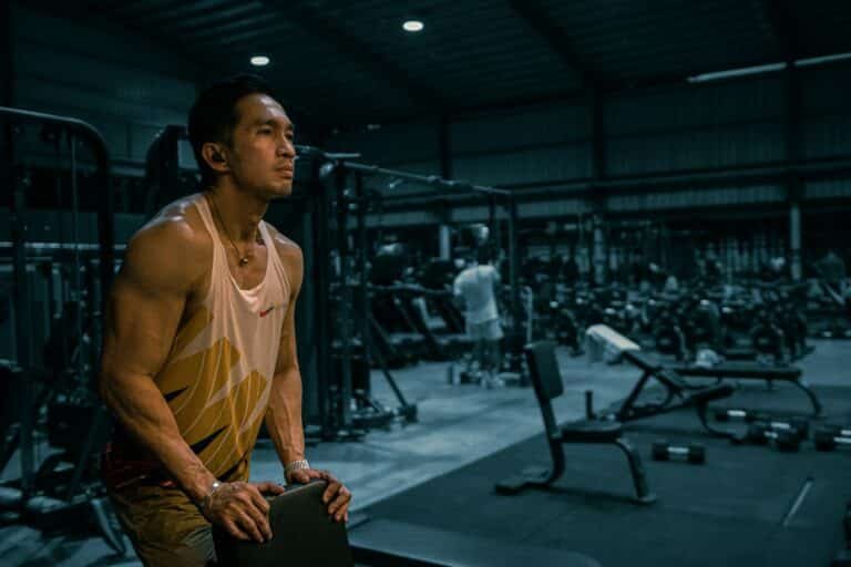 Man in a tank top resting between sets in a large gym
