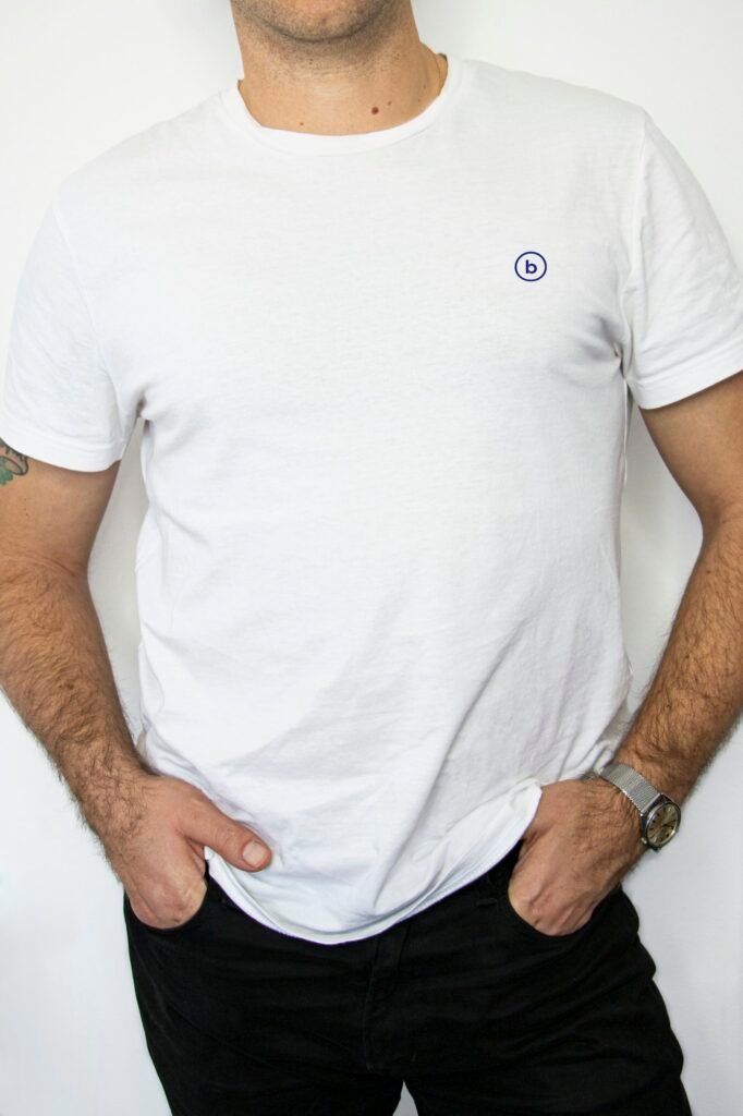 Man in a white crew neck t-shirt and dark jeans with his hands in his pockets