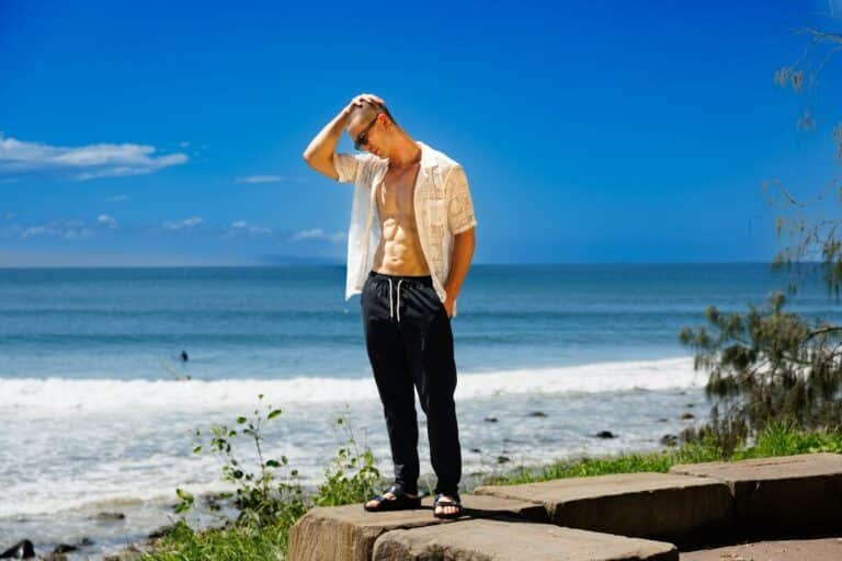 Man in an open white shirt and black pants on a coastal cliff