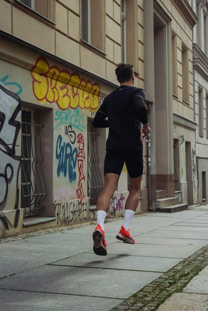 Man in black shorts and a black shirt jogging on a sidewalk