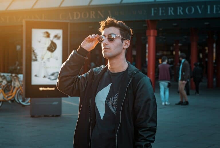 Man in sunglasses and a black zip-up jacket outside a train station